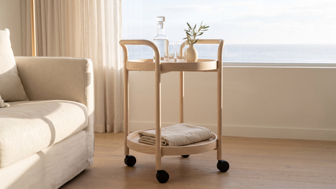 A round pale ash bar cart used as a side table beside a linen sofa in a light-filled Perth apartment