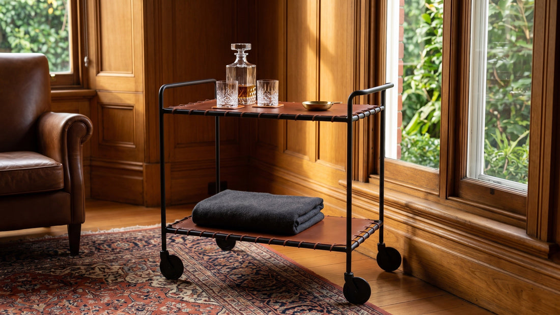 A black iron and chestnut leather two-tier bar cart with clear glassware in a timber-panelled Hawthorn study