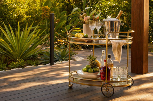 Outdoor bar cart Australia — gold oval bar cart styled on a timber alfresco deck with tropical greenery and champagne bucket
