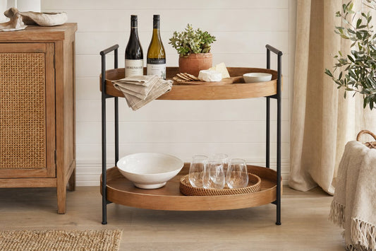 Wooden bar cart Australia — round timber shelves with black iron frame styled with wine bottles and glassware in a coastal Hamptons interior