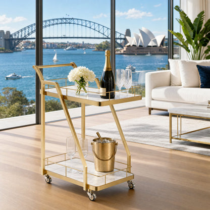 The Mosman Two-Tier Gold Marble-Look Service Cart featuring a striking Z-frame and white faux-marble shelves, styled with wine and glasses and day spas.