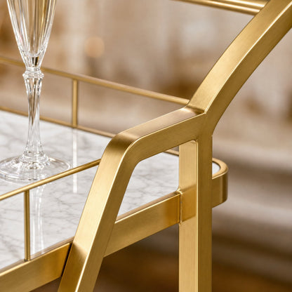 The Mosman Two-Tier Gold Marble-Look Service Cart featuring a striking Z-frame and white faux-marble shelves, styled with wine and glasses and day spas.