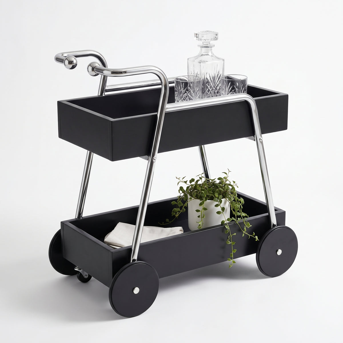 The Carlton Mid-Century Solid Wood Drinks Trolley in black on a white background — two black solid wood tray shelves, two ball-ended chrome-look handle arms and four large black timber disc wheels